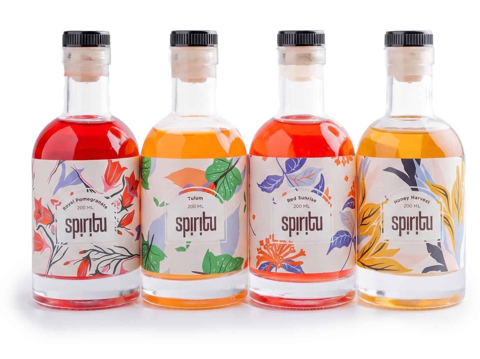 בארבע בקבוקי קוקטיילים צבעוניים של SPIRITU עם תוויות פרחוניות.
